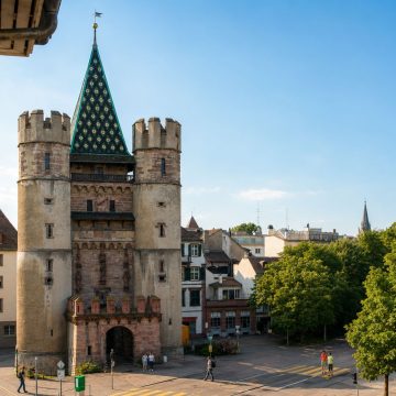 Protegido por duas formidáveis torres redondas e coroado por telhados de azulejos coloridos, este magnífico portão do século XIV é considerado a fortificação medieval mais bem preservada da Suíça e uma grandiosa porta de entrada histórica para Basileia.