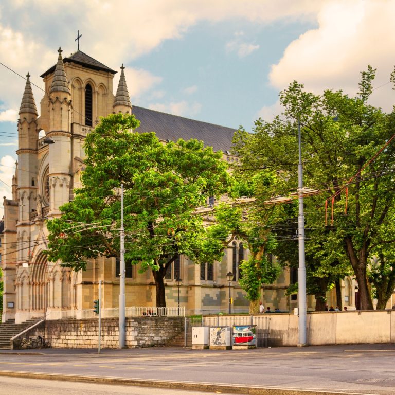 Caça ao tesouro e visita autoguiada a Genebra 6 A Basílica de Notre-Dame de Genebra é a principal igreja católica da cidade, apresentando um design neoclássico deslumbrante que contrasta elegantemente com a história da Reforma da cidade. Construída em meados do século XIX, é célebre pelos seus notáveis vitrais e pela sua atmosfera pacífica e espiritual, localizada perto da movimentada estação ferroviária principal.