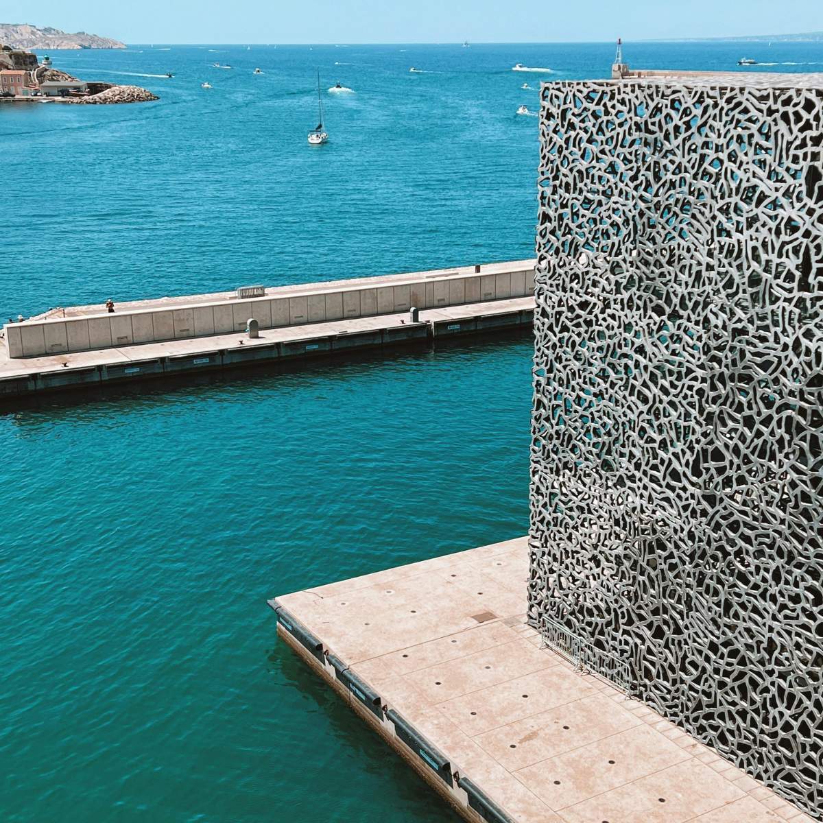 Jeu de piste et visite libre à Marseille 4 Le Mucem est un majestueux musée contemporain où une grande façade de béton en forme de dentelle et une passerelle panoramique créent un pont monumental entre l'histoire méditerranéenne et l'architecture moderne.