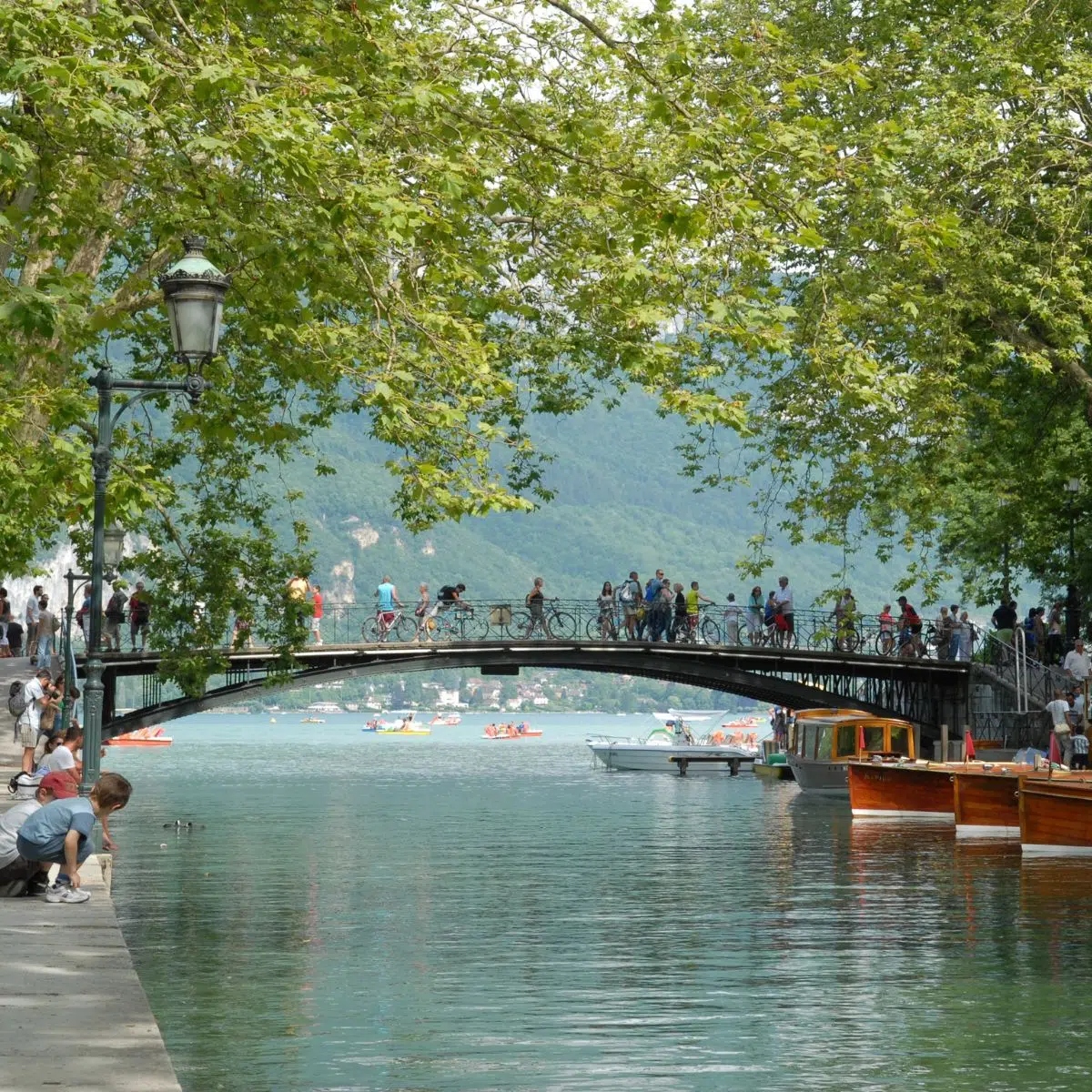 Caccia al tesoro e tour autoguidato ad Annecy 3 Affacciato sul pittoresco canale dove le acque cristalline del Thiou si riversano nel lago, questo iconico ponte in ferro offre un punto panoramico di grande romanticismo, incorniciato da un maestoso paesaggio alpino e da alberi sospesi.