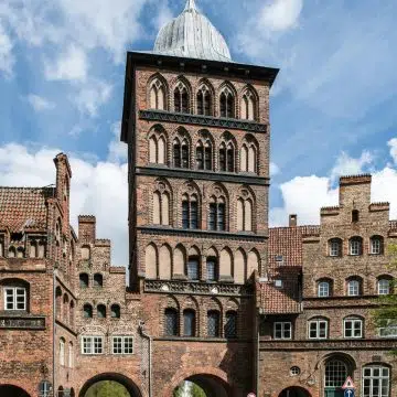Il Burgtor è la porta settentrionale della città vecchia anseatica di Lubecca, una formidabile struttura tardo-gotica in mattoni che un tempo sorvegliava lo stretto ingresso terrestre all'isola. La sua imponente torre con cupola in bronzo e le sue storiche mura di difesa offrono uno sguardo potente sull'importanza militare medievale della città e sul suo duraturo patrimonio architettonico.