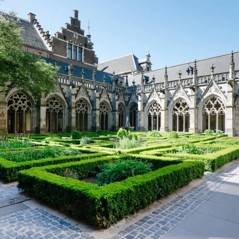 Juego de pistas y visita autoguiada por Utrecht 6 El Pandhof van de Dom es un impresionante jardín claustral del siglo XIV que conecta la catedral con la universidad y sirve de apacible santuario decorado con intrincada cantería gótica. Está considerado uno de los patios más bellos de Holanda, con un exuberante jardín de hierbas y ornamentadas pasarelas arqueadas que ilustran la rica historia eclesiástica de Utrecht.