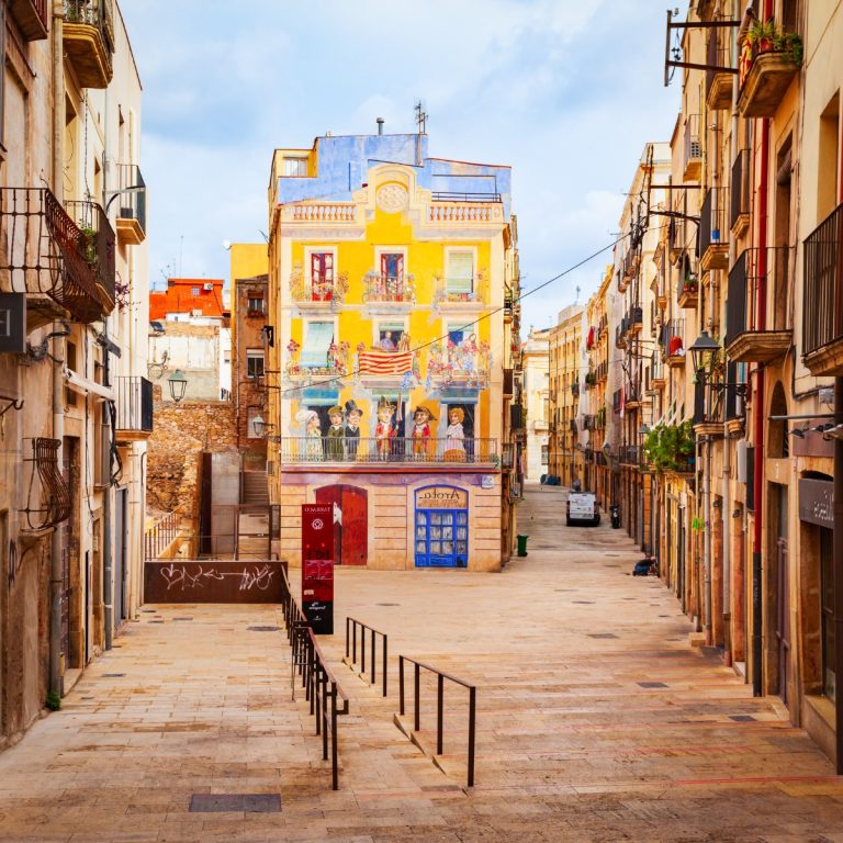 Plaça dels Sedassos is de thuisbasis van een van Tarragona's beroemdste muurschilderingen, een levendige trompe-l'oeil die een traditionele 19e-eeuwse gevel tot leven brengt met kleurrijke lokale personages. Dit charmante plein mengt straatkunst naadloos met geschiedenis en biedt een speelse blik op de mediterrane ziel en het architectonische erfgoed van de stad.