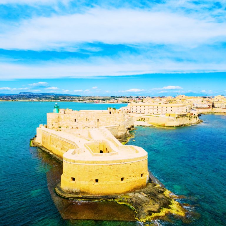 Búsqueda del tesoro y recorrido autoguiado por Siracusa 2 Castello Maniace es una formidable ciudadela del siglo XIII situada en la punta de la isla de Ortigia, que se alza como un majestuoso centinela sobre las aguas turquesas del puerto de Siracusa.