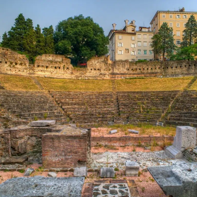 Caça ao tesouro e visita autoguiada a Trieste 5 O Teatro Romano de Trieste é uma antiga arena notavelmente preservada, que remonta ao século I d.C., onde os espectadores se reuniam para assistir a espectáculos com o Mar Adriático como pano de fundo.