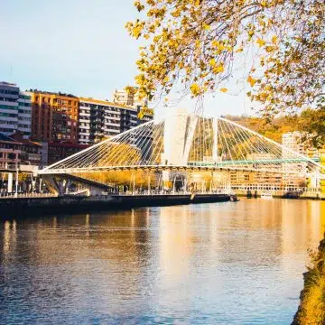 The Zubizuri Bridge is a majestic modern landmark where a grand curved walkway and soaring white arches create a monumental path over the Nervión River.