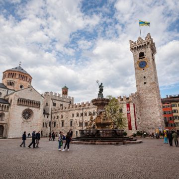 Piazza del Duomo to eleganckie serce Trydentu, otoczone zabytkowymi pałacami, kawiarniami i kultową katedrą w Trydencie, z piękną fontanną Neptuna tworzącą żywą i malowniczą atmosferę pod alpejską panoramą.
