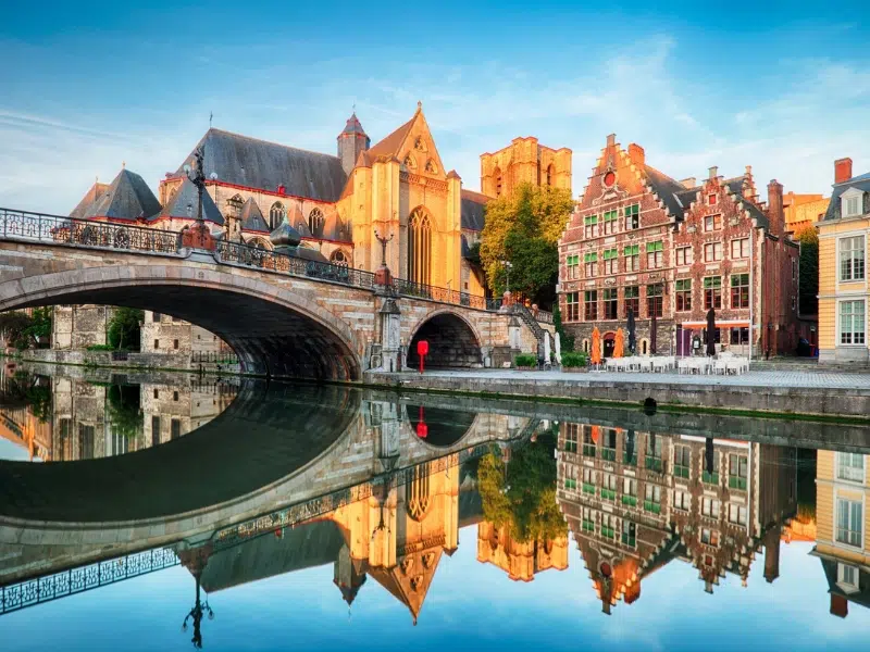 Panoramic view from Sint-Michielsbrug in Ghent, showcasing the iconic medieval “three towers” – St. Nicholas' Church, the Belfry, and St. Bavo's Cathedral – along with historic buildings and the Leie River.