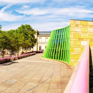 Neue Staatsgalerie to postmodernistyczne arcydzieło architektury zaprojektowane przez Jamesa Stirlinga, słynnie łączące kolorowe, zaawansowane technologicznie elementy z klasyczną kamieniarką, aby pomieścić jedną z najbardziej prestiżowych kolekcji sztuki w Niemczech.