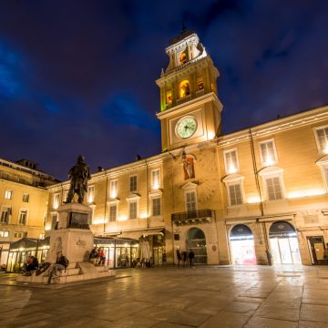 Piazza Garibaldi serves as the vibrant social heart of Parma, where the illuminated Governor's Palace and its historic bell tower overlook a lively square filled with elegant cafés and neoclassical architecture.